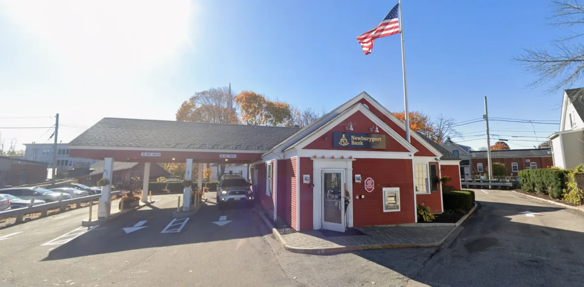 A small red building with a Northport Bank sign, drive-thru lanes, and a U.S. flag on a pole outside, under a clear blue sky.