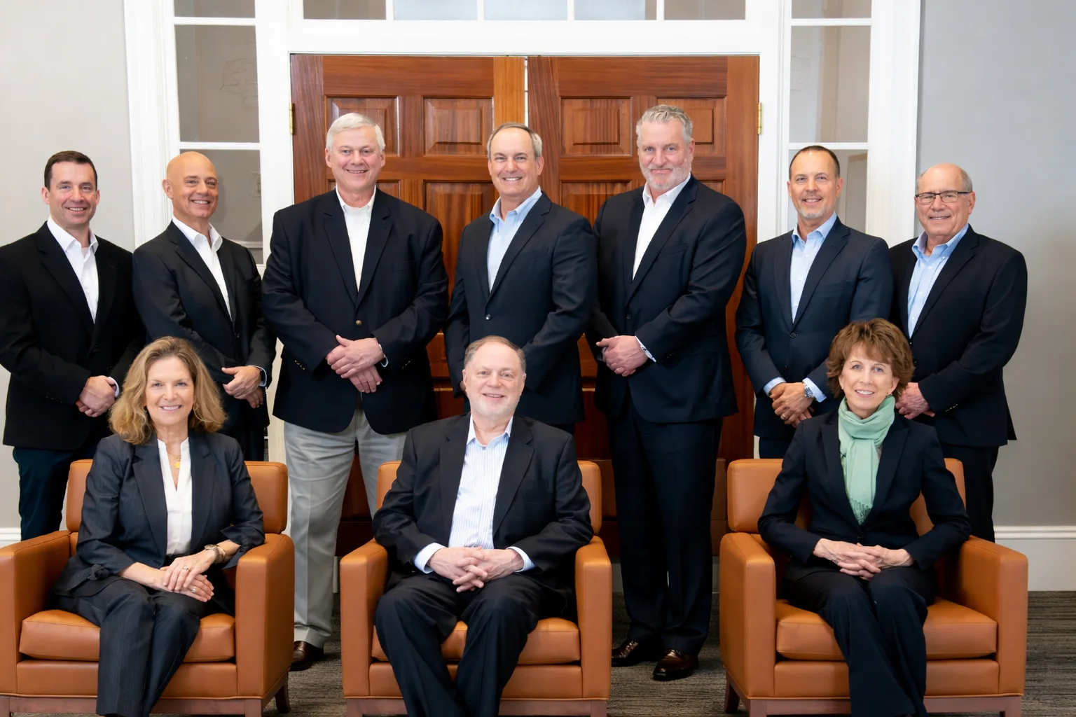 Ten business professionals from a community bank in Massachusetts pose for a group photo in a formal office, smiling before wooden doors—seven stand, three sit in front.
