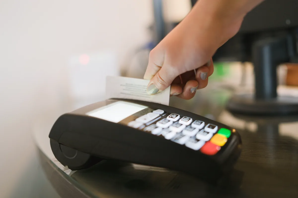 A person swipes a card through a credit card payment terminal on a glass surface.