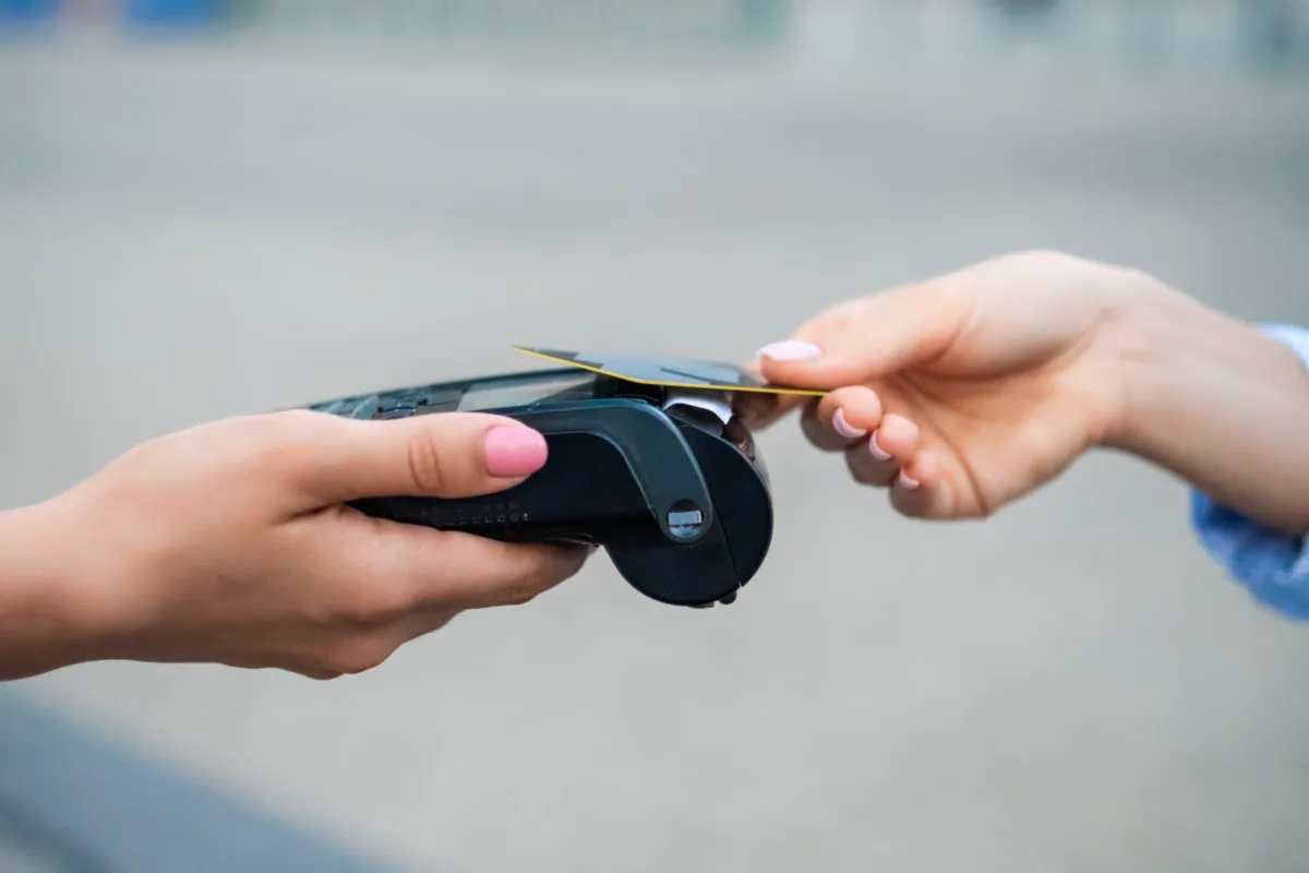 A person holds a payment terminal while another person pays by tapping a credit card on it for contactless payment.
