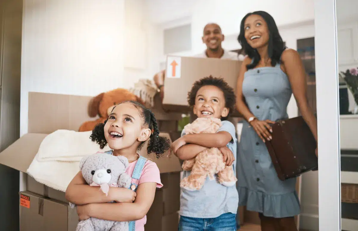 Two smiling children hold stuffed animals in front of moving boxes, with two adults behind them, as a family moves into their new home with help from Newburyport Bank mortgage lenders.