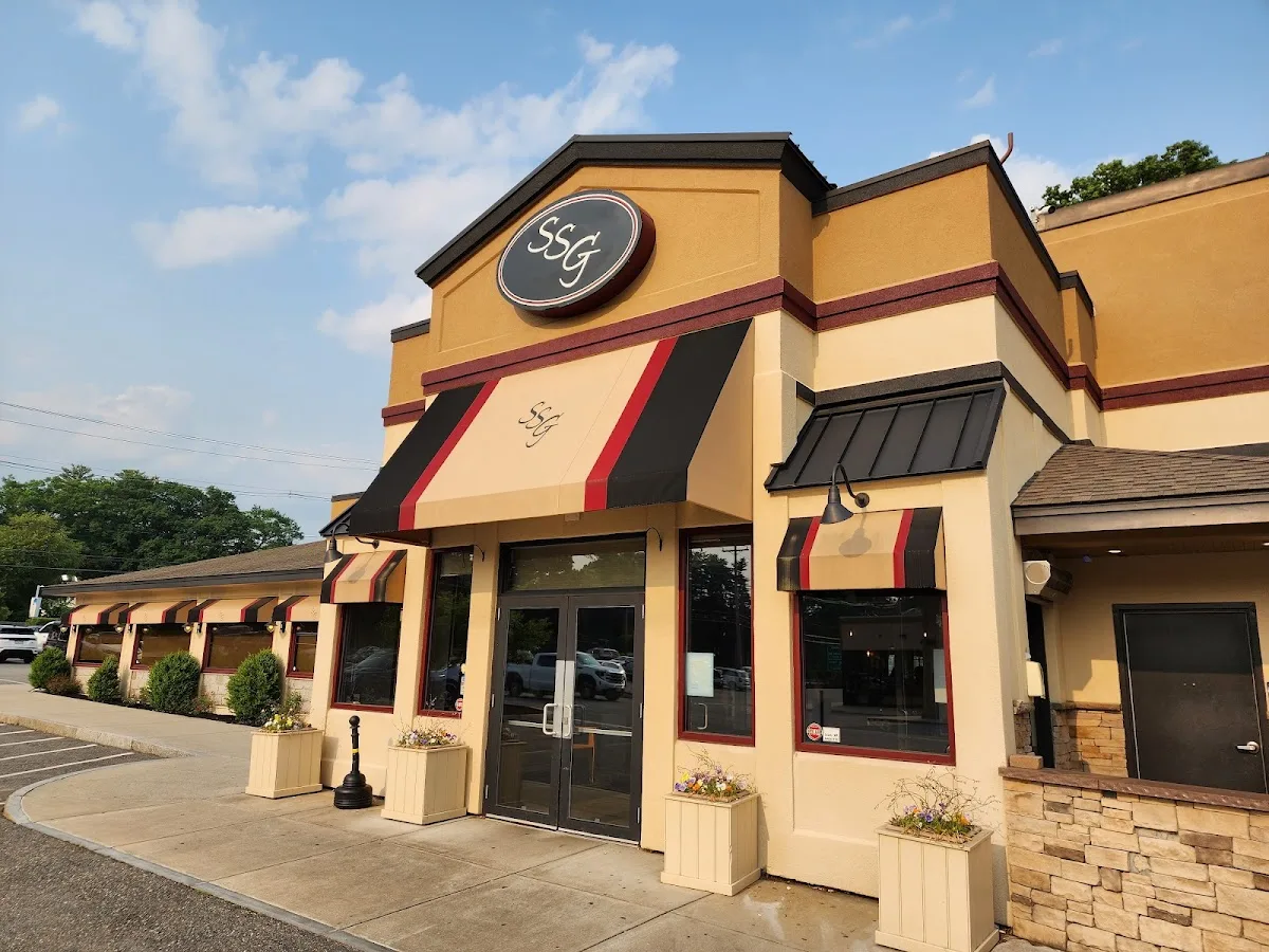 A tan building with black and red striped awnings, glass doors, and a round “SSG” sign above the entrance, near Newburyport Bank by the river on a sunny day.